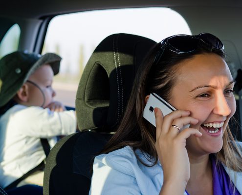 Frau lacht mit Handy am Steuer