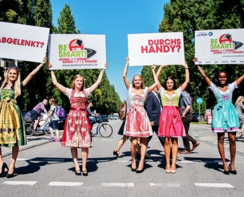 5 Mädchen in Dirndl halten auf einer Straße Schilder in die Luft