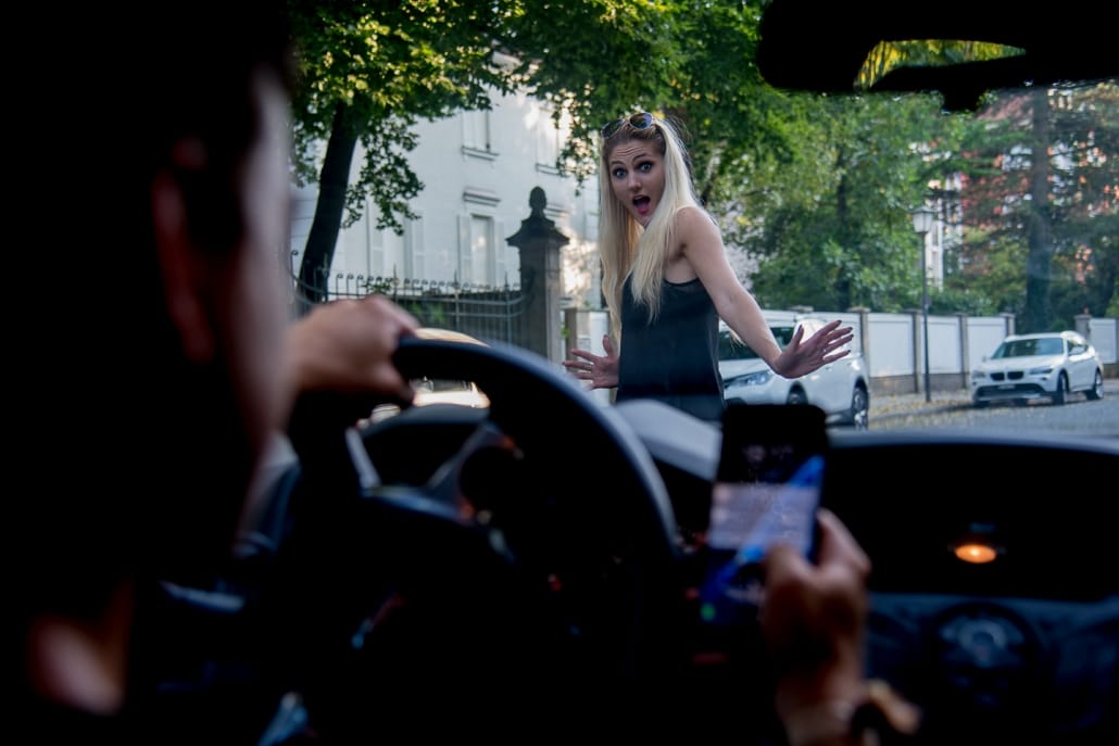 Ein Mann mit Handy am Steuer übersieht eine blonde Frau auf der Straße