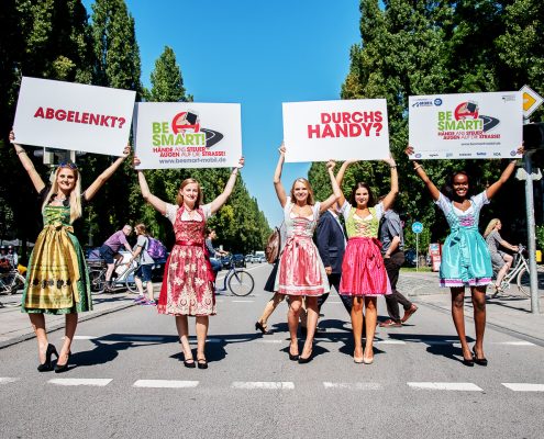 5 Mädchen in Dirndl halten auf einer Straße Schilder in die Luft