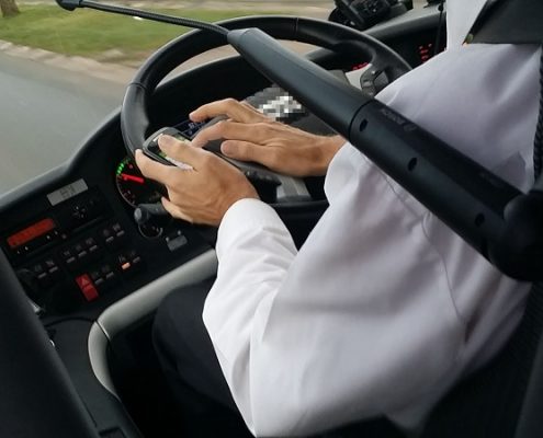 Mann am Steuer eines Linienbusses, tippt auf seinem Smartphone