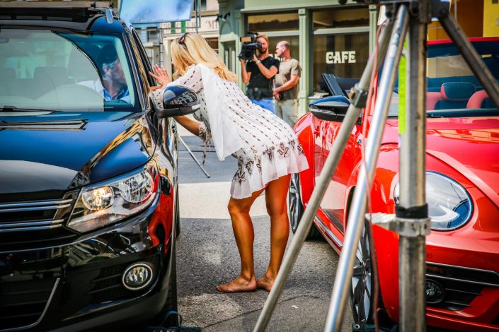 Ein im Auto sitzender Mann und eine blonde Frau auf der Straße sehen sich an