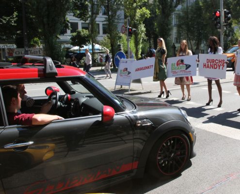 Vier Mädchen in Dirndl und Schildern in der Hand halten die Autos auf der Straße an