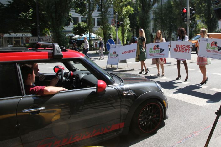 Vier Mädchen in Dirndl und Schildern in der Hand halten die Autos auf der Straße an