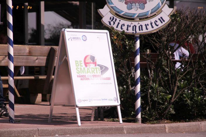 Ein Plakatehalter auf dem Bordstein vor einem Münchner Biergarten