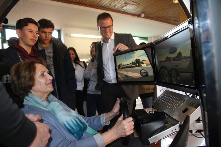 Eine Frau benutzt den Fahrsimulator und Kinder und Michael Haberland zu ihrer Linken sehen ihm zu