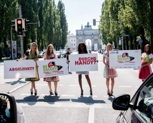 5 Mädchen in Dirndl halten auf einer Straße Schilder in den Händen