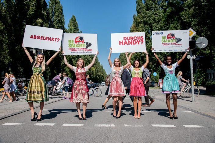 5 Mädchen in Dirndl halten auf einer Straße Schilder in die Luft