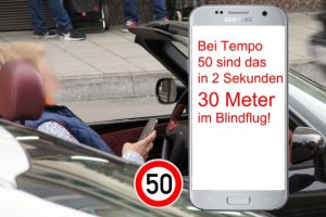 Person am Steuer eines Cabrios hält Smartphone in der Hand