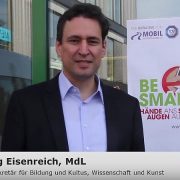 Ein Herr redet in eine Kamera mit BeSmart Plakat