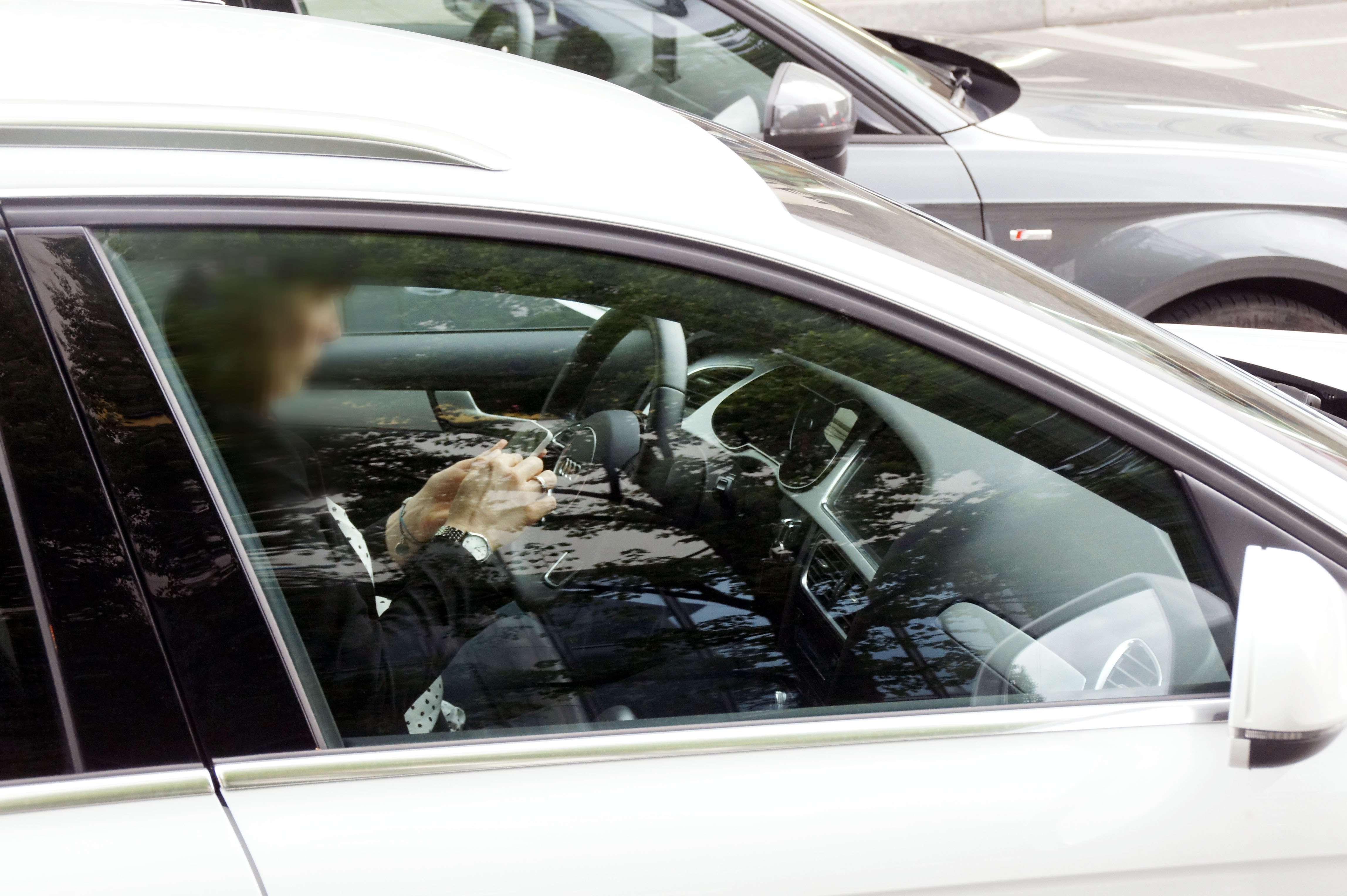 Eine Person (Gesicht unkenntlich) fährt in seinem Auto mit Handy am Steuer