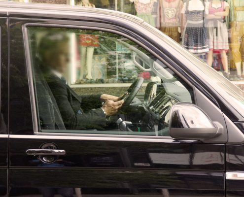 Eine Person (Gesicht unkenntlich) fährt in seinem Auto mit Handy am Steuer