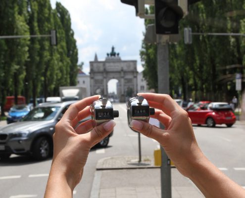 Zwei Hände halten jeweils einen Verkehrszähler, im Hintergrund eine belebte Straße