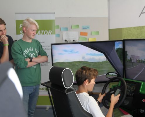 Ein Junge fährt mit dem Fahrsimulator und weitere sehen zu