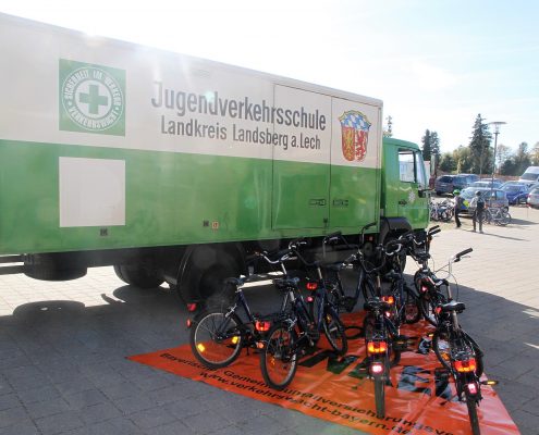 Ein grüner, großer Laster der Jugendverkehrsschule Landkreis Landsberg a. Lech auf einem Parkplatz und einigen Fahrrädern die vor diesem stehen