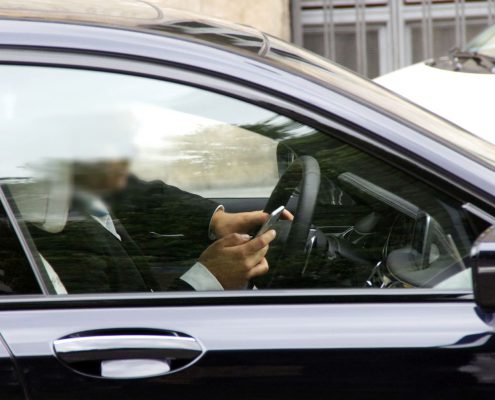 Mann mit Handy am Steuer eines schwarzen Wagens