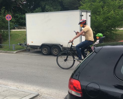 Fahrradfahrer mit Kind im Kindersitz und Handy in der Hand